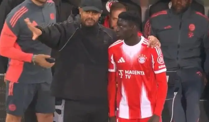 Coach in black cap and hoodie with arm around a player in a red-and-white striped soccer kit on the sideline area. Coach in black cap and hoodie with arm around a player in a red-and-white striped soccer kit on the sideline area.