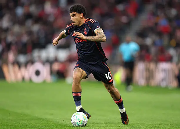 Soccer player in a dark navy uniform with orange trim dribbling a white ball on a green pitch during a match. Soccer player in a dark navy uniform with orange trim dribbling a white ball on a green pitch during a match.