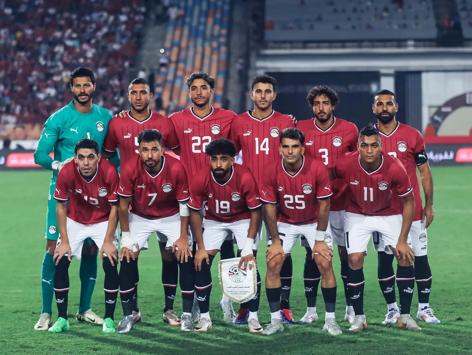 Egyptian national football team posing in red jerseys on the field with goalie in green at left.