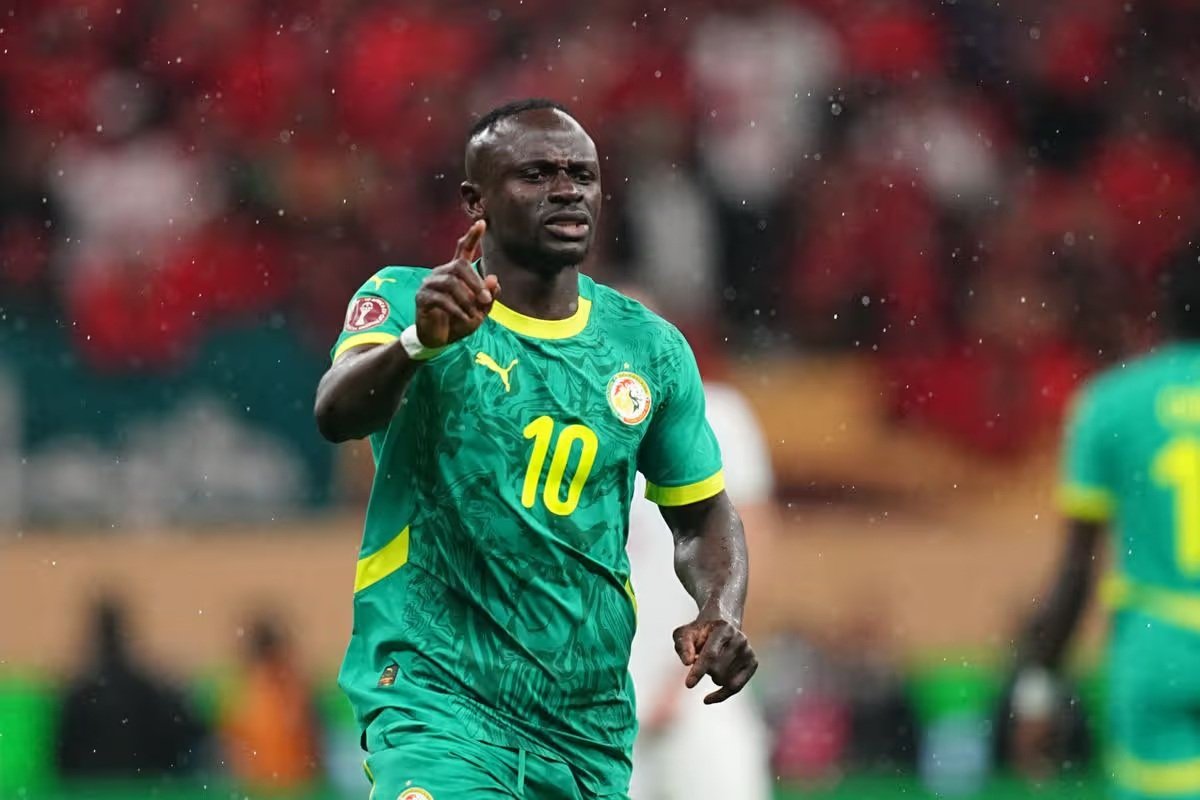 Senegal national team footballer in green kit with number 10 celebrating on the rain-soaked pitch, raising one finger.