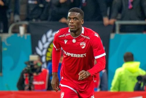 Soccer player in a red kit running on the field during a match on a stadium pitch.