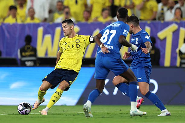 Soccer player in a yellow jersey dribbles the ball while two blue-clad defenders move in on him on the field.