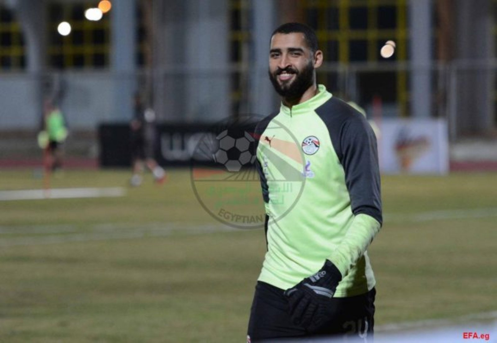 Goalkeeper in neon green jersey smiles on a soccer field with blurred background. Goalkeeper in neon green jersey smiles on a soccer field with blurred background.
