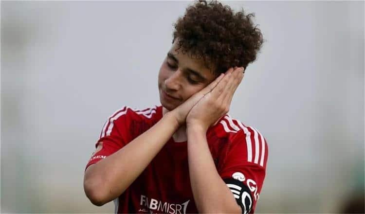 Young soccer player in a red jersey rests his head on clasped hands, eyes closed as if sleeping or resting.