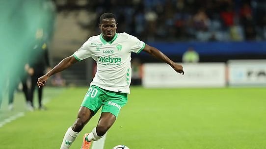 Soccer player in a white and green kit dribbling the ball on a grassy pitch during a match, number 20 visible .
