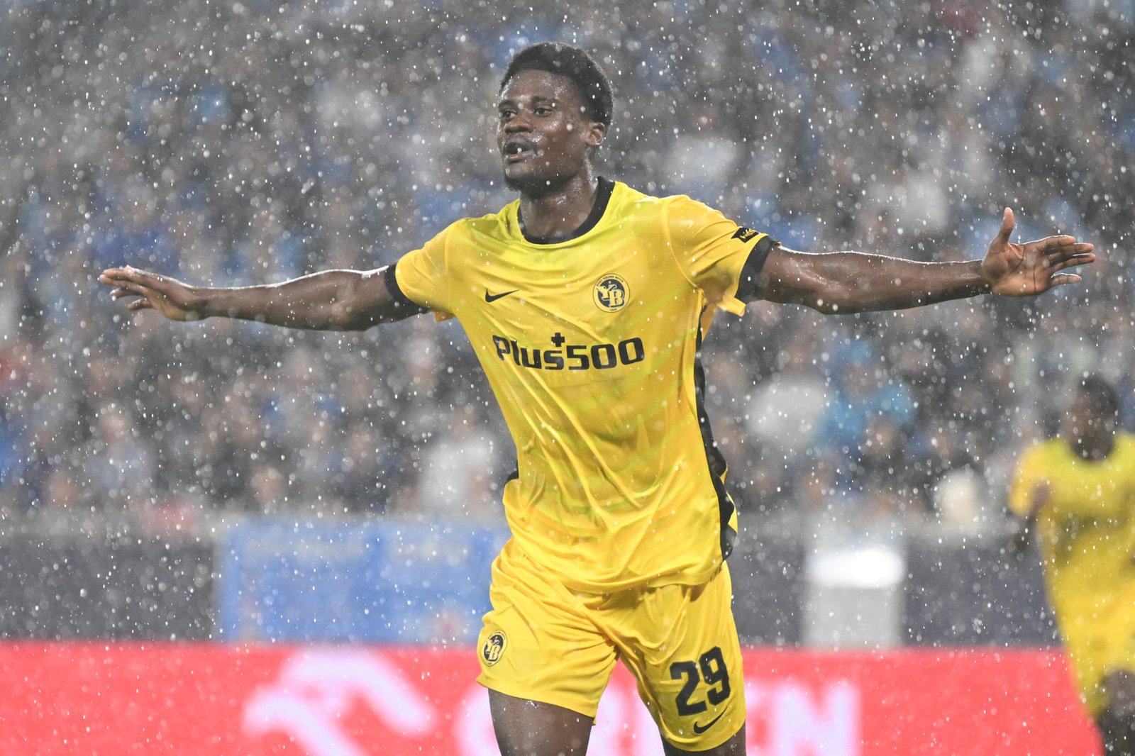 Soccer player in a yellow kit with arms outstretched celebrate in a snowy stadium. Soccer player in a yellow kit with arms outstretched celebrate in a snowy stadium.