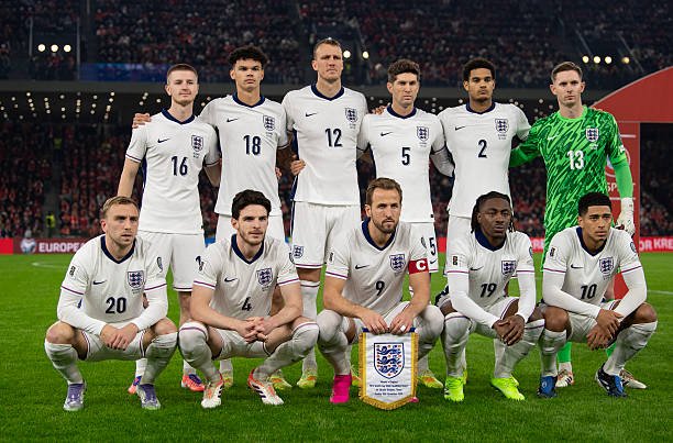 England men's national football team lineup posing on the pitch: 11 players in white kits, goalkeeper in green, team captain at center with a shield.