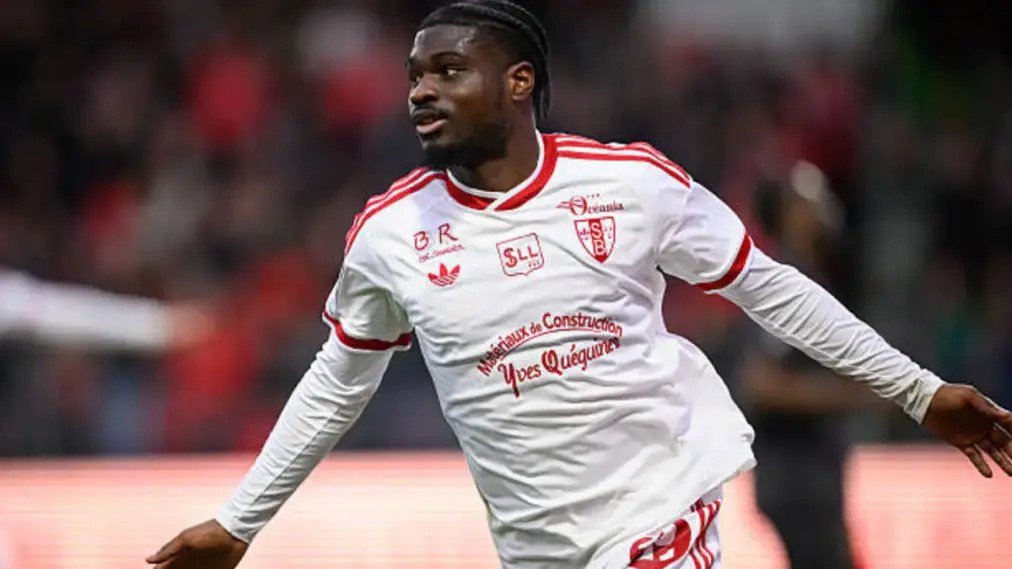 Soccer player in a white jersey with red trim running on the field, blurred crowd in the background.