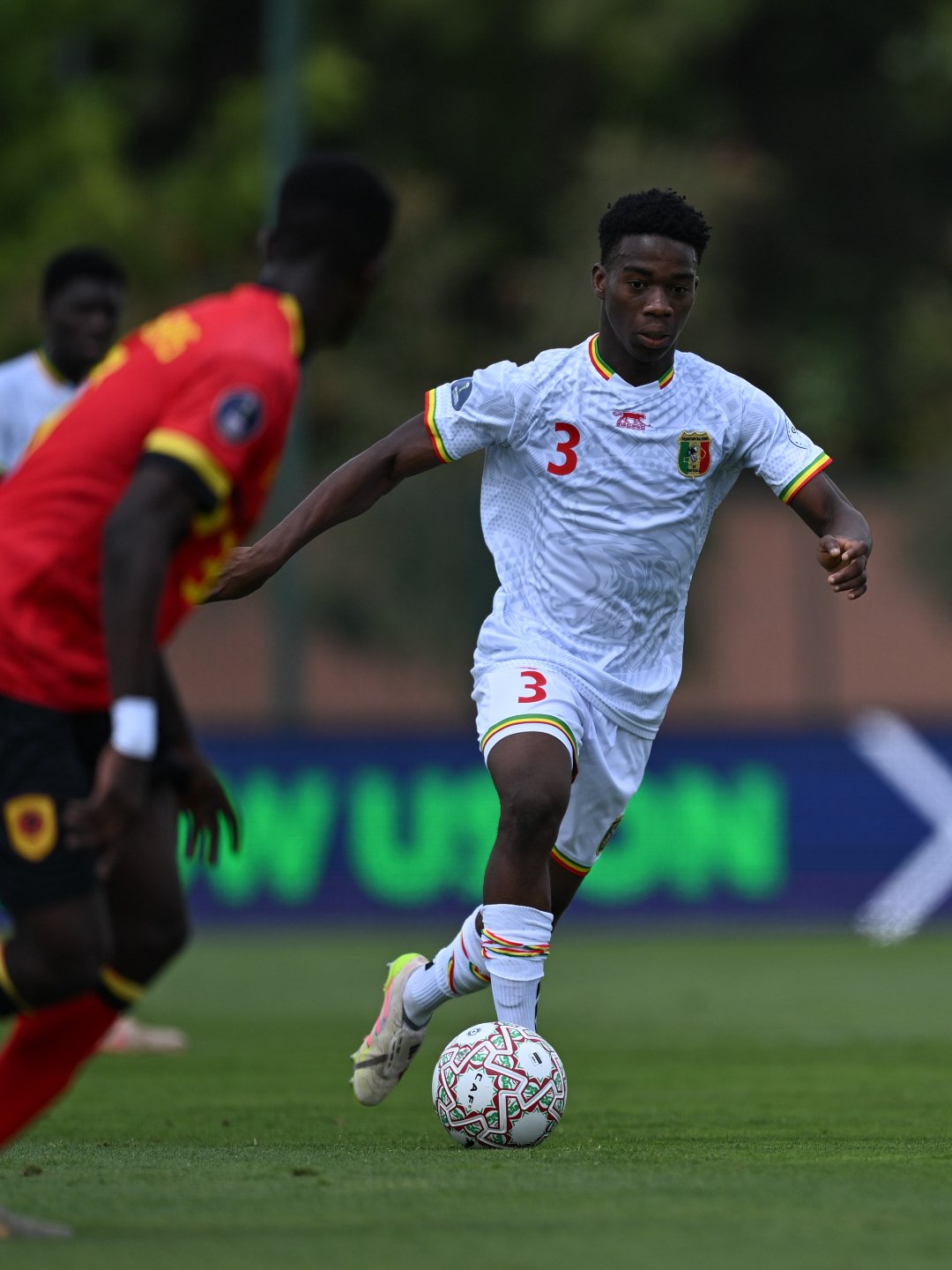 Soccer player in a white jersey with number 3 dribbling the ball on a green pitch during a match. Soccer player in a white jersey with number 3 dribbling the ball on a green pitch during a match.