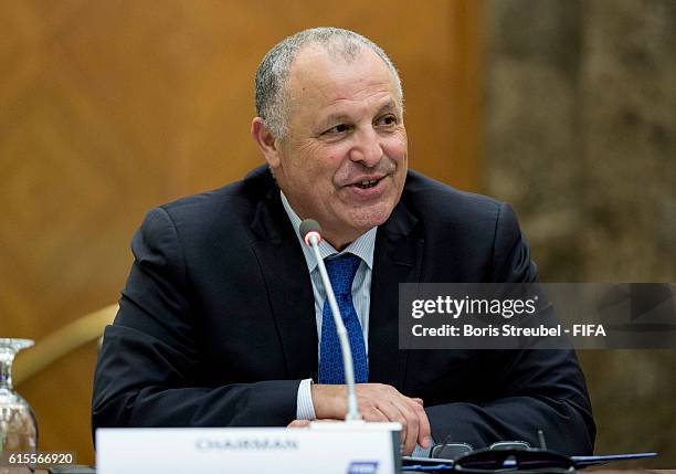 Middle-aged man in a dark suit and blue tie speaks into a microphone at a formal panel event.