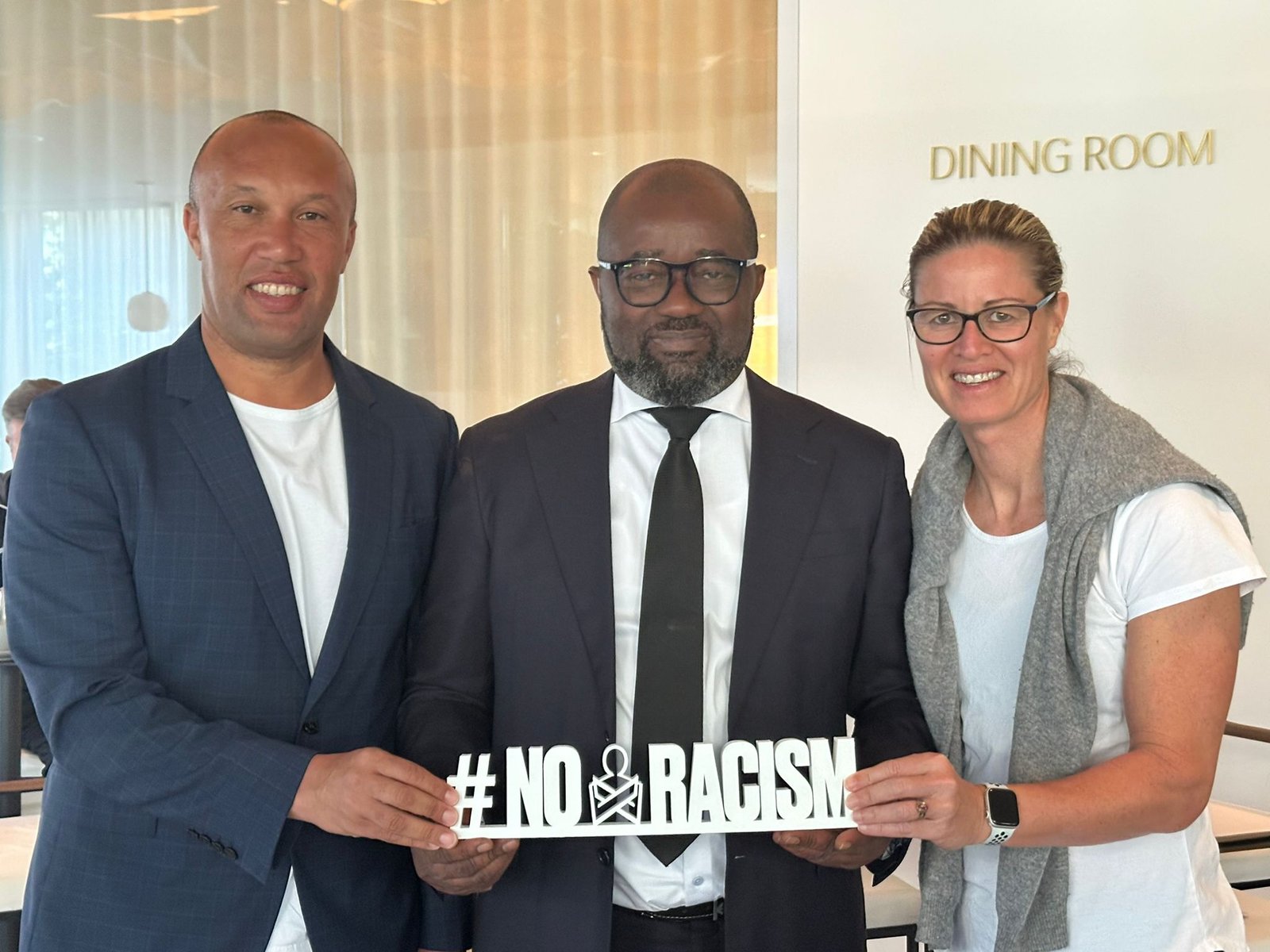 Three adults posing together indoors, holding a sign that reads '# NO RACISM' to promote anti-racism. Three adults posing together indoors, holding a sign that reads '# NO RACISM' to promote anti-racism.