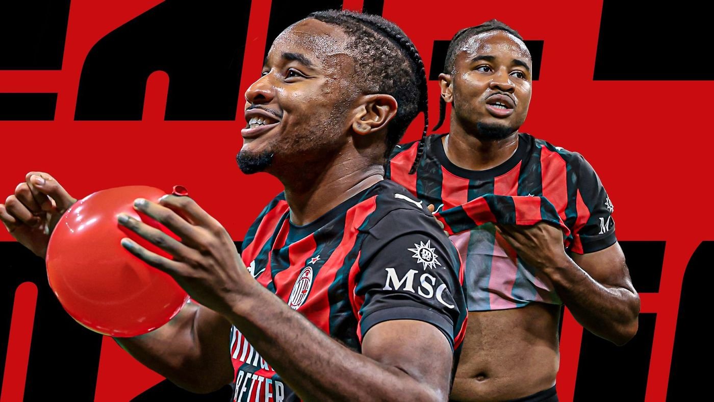 Two soccer players in red-and-black striped jerseys celebrate; one holds a red ball while the other hugs him, against a bold red and black background.