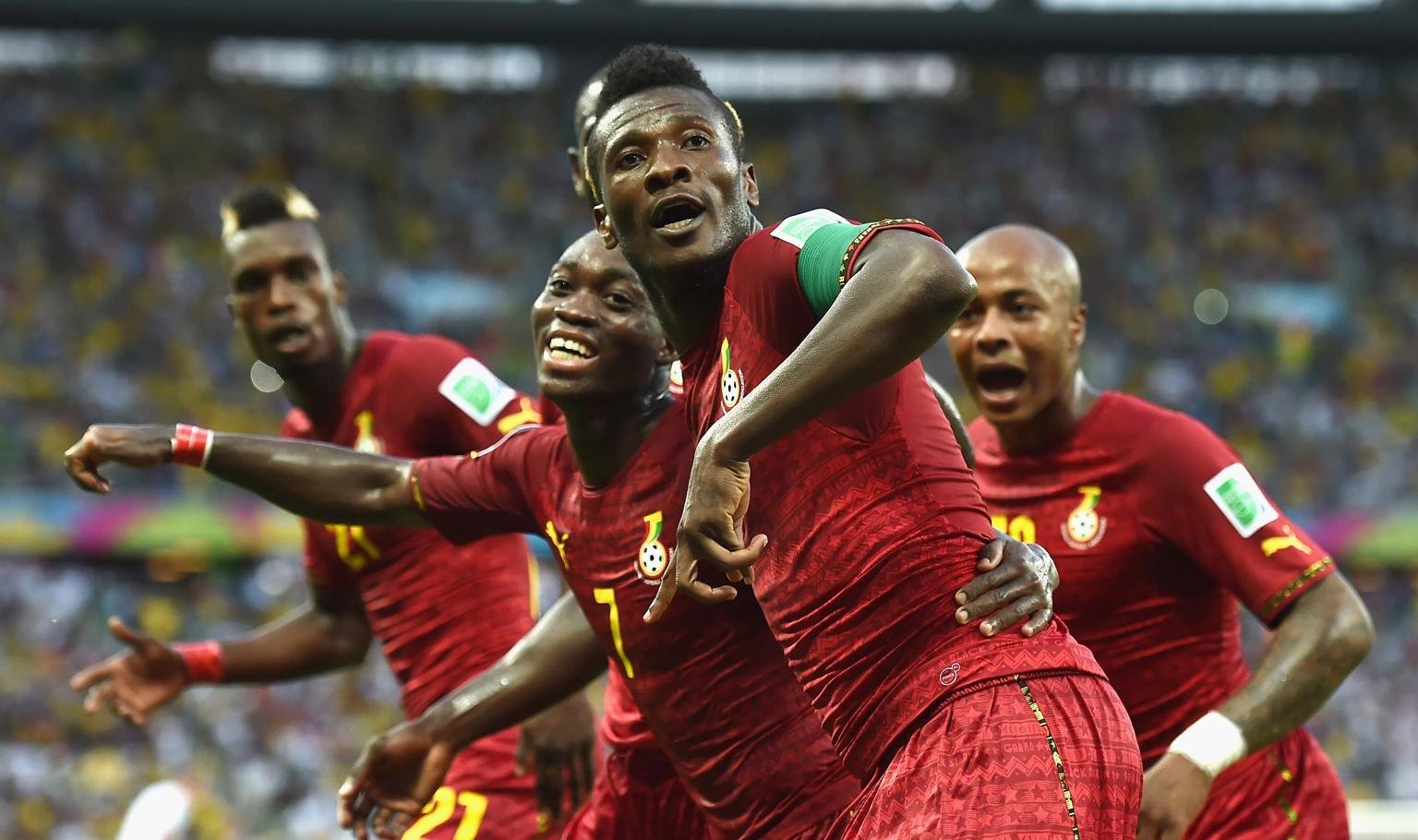 Ghana national team players celebrate a goal, wearing red jerseys on a crowded stadium field. Ghana national team players celebrate a goal, wearing red jerseys on a crowded stadium field.