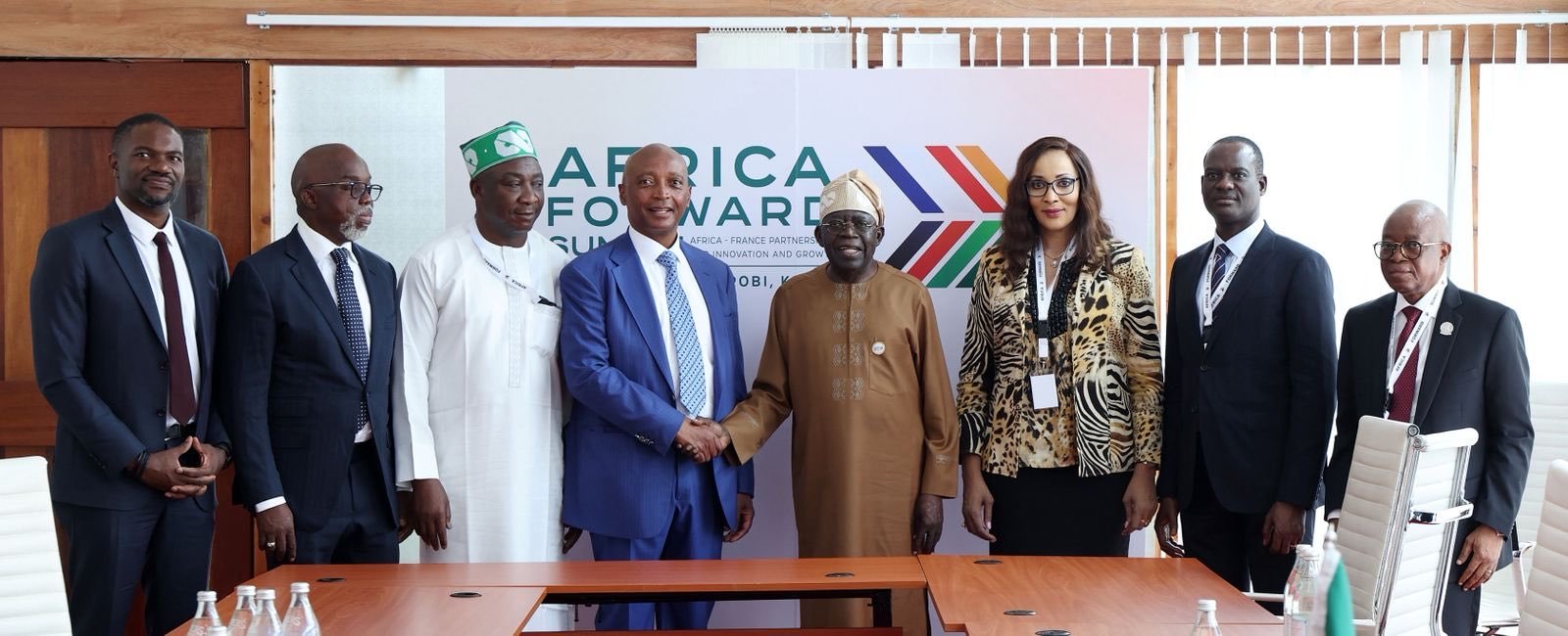 Eight professionals in formal attire pose for a photo in a conference room, with two men shaking hands in front of an 'Africa Forward' banner. Eight professionals in formal attire pose for a photo in a conference room, with two men shaking hands in front of an 'Africa Forward' banner.