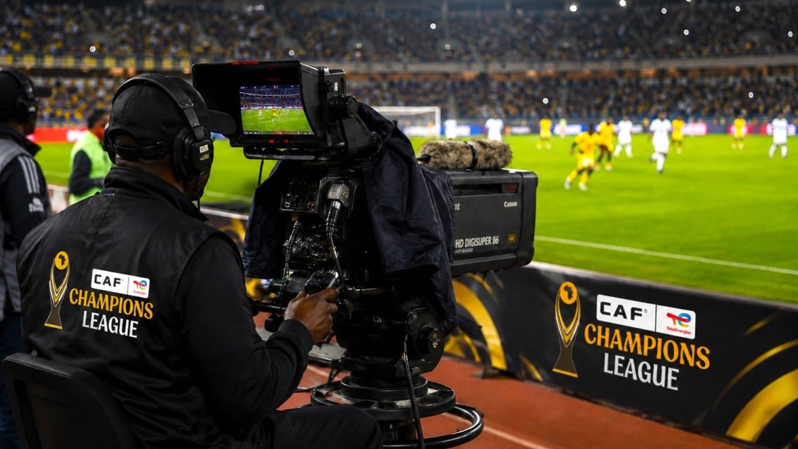 Cameraman filming a soccer match for CAF Champions League from the sideline camera station with a large broadcast camera and headphones on.