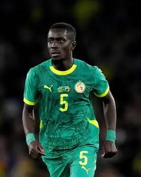 Male soccer player in a green kit with yellow trim and the number 5, mid-stride on the field.