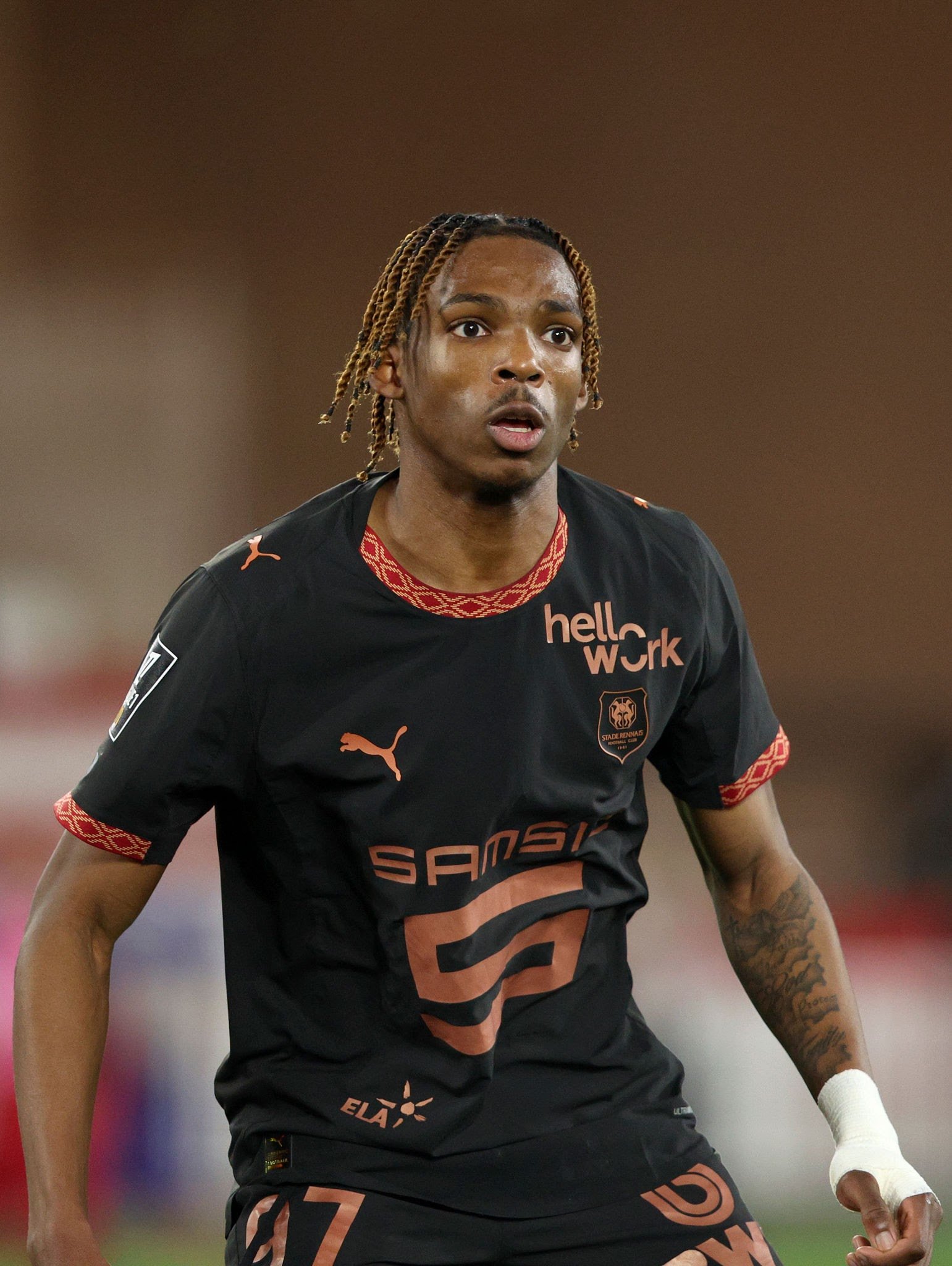 Soccer player with braided hair in a dark jersey on the field, looking focused during a match.
