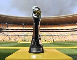 Sports trophy with a curved black and gold design on a yellow pedestal, set on a field with a stadium backdrop.