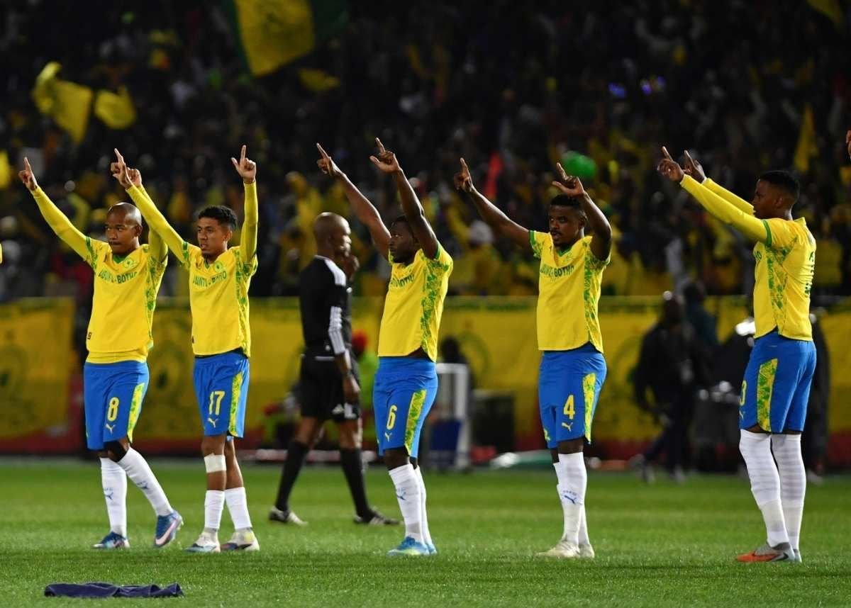 Five football players in yellow jerseys and blue shorts stand in a line on the field, arms raised in celebration. A referee and a crowd are in the background. Five football players in yellow jerseys and blue shorts stand in a line on the field, arms raised in celebration. A referee and a crowd are in the background.