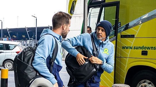 Two men with backpacks boarding a yellow bus; one man helps the other in a wheelchair into the bus door.