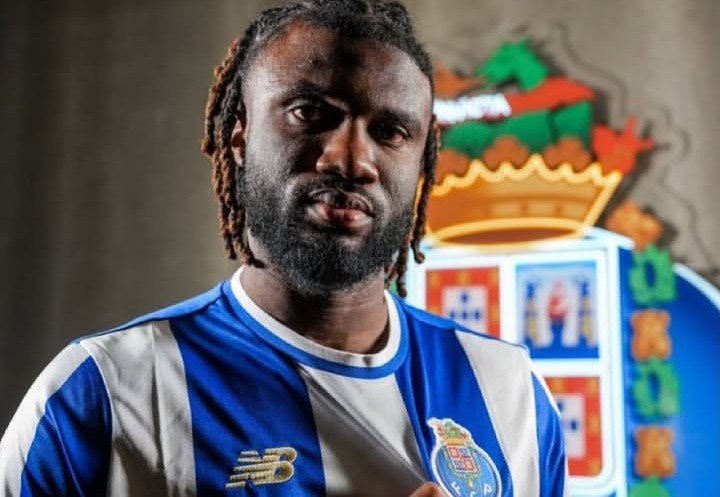 Portrait of a man with braided hair and a beard wearing a blue and white striped soccer jersey, standing in front of a colorful crest backdrop