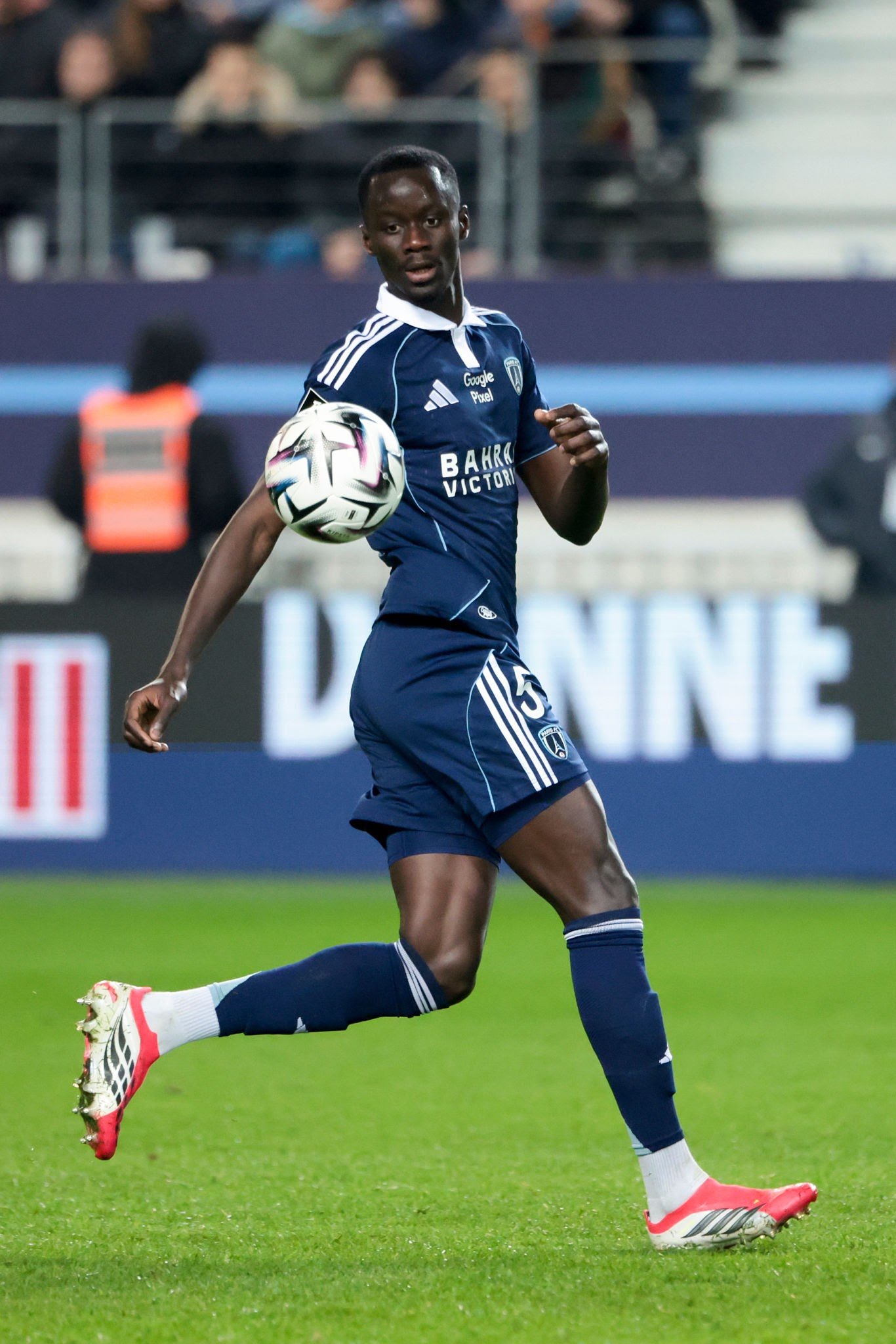 Soccer player in dark blue uniform controls a ball on a grassy pitch during a match, stadium in background. Soccer player in dark blue uniform controls a ball on a grassy pitch during a match, stadium in background.