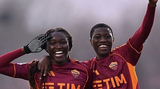 Two teammates celebrate together, smiling with arms around each other in maroon uniforms on a field Two teammates celebrate together, smiling with arms around each other in maroon uniforms on a field