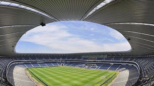 Panoramic view of a modern empty soccer stadium with a curved roof and green pitch