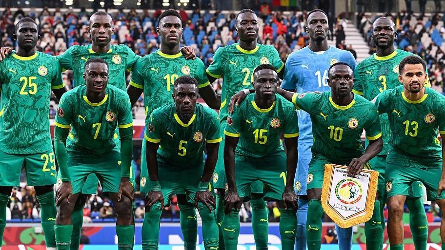 Group photo of the Cameroon national football team in green kits posing on the field with a stadium crowd behind them. Group photo of the Cameroon national football team in green kits posing on the field with a stadium crowd behind them.