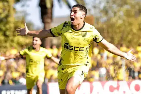 Soccer player in a bright yellow kit celebrates with arms wide open on the field, fans blurred in the background. Soccer player in a bright yellow kit celebrates with arms wide open on the field, fans blurred in the background.