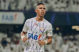 Male soccer player in a white striped jersey with blue sponsor lettering runs on the field during a match, with a stadium crowd in the background. Male soccer player in a white striped jersey with blue sponsor lettering runs on the field during a match, with a stadium crowd in the background.