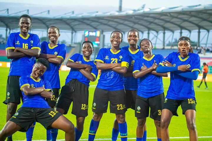 Seven soccer players in blue jerseys with yellow trim pose together on a stadium field, arms crossed and smiling at the camera. Seven soccer players in blue jerseys with yellow trim pose together on a stadium field, arms crossed and smiling at the camera.