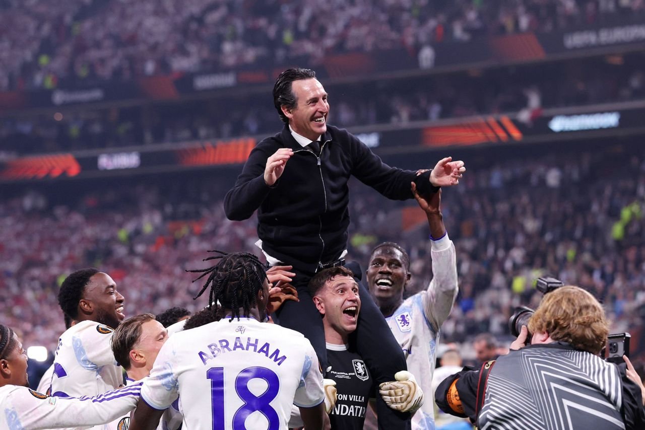 Soccer players lift a man on their shoulders in a jubilant celebration on the field.