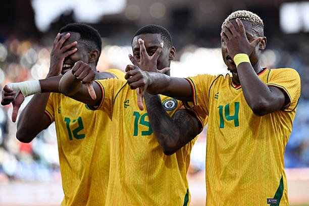 Three soccer players in yellow jerseys celebrate, each with a hand over their face or eyes as they stand together on the field.