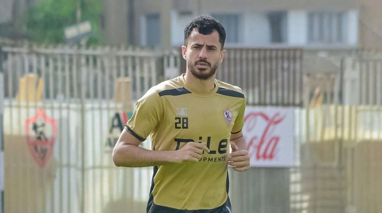 Male soccer player in a gold jersey running on a training field, with banners and a Coca-Cola sign in the background.
