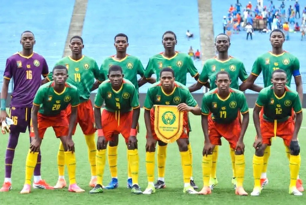 A men's soccer team lined up for a pre-game photo on a green field, wearing green jerseys with yellow shorts, with a goalkeeper in purple on the left and one player holding a club banner in the center.