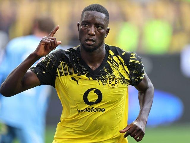 Portrait of a Borussia Dortmund footballer in the yellow‑black home kit, pointing finger up in celebration on the pitch.