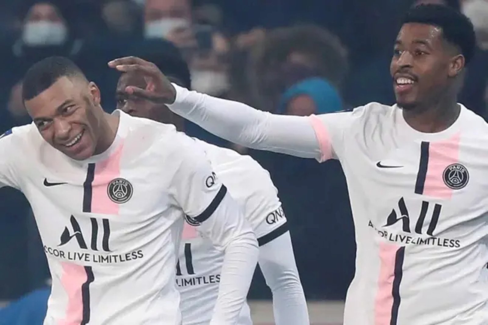 Two PSG players celebrate on the pitch, smiling as one pats the other on the back in white kits with pink accents. Two PSG players celebrate on the pitch, smiling as one pats the other on the back in white kits with pink accents.
