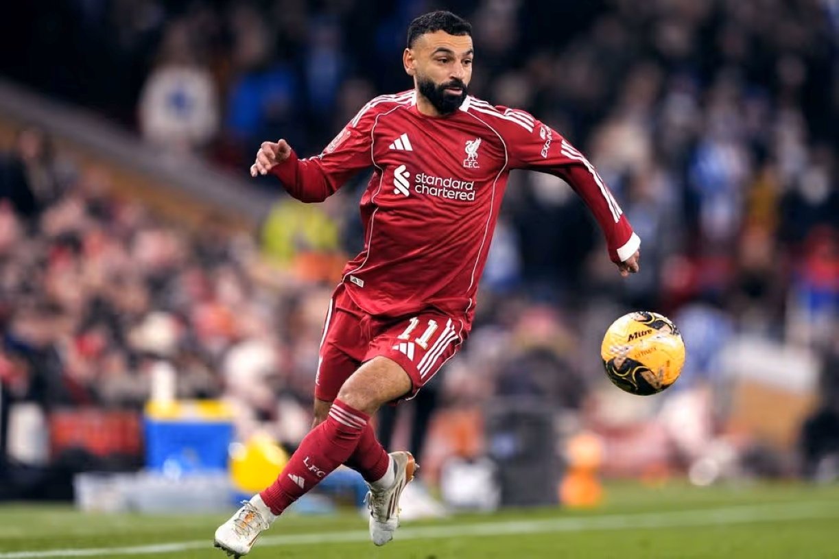 Soccer player in red Liverpool kit kicking a yellow ball during a match, mid-action