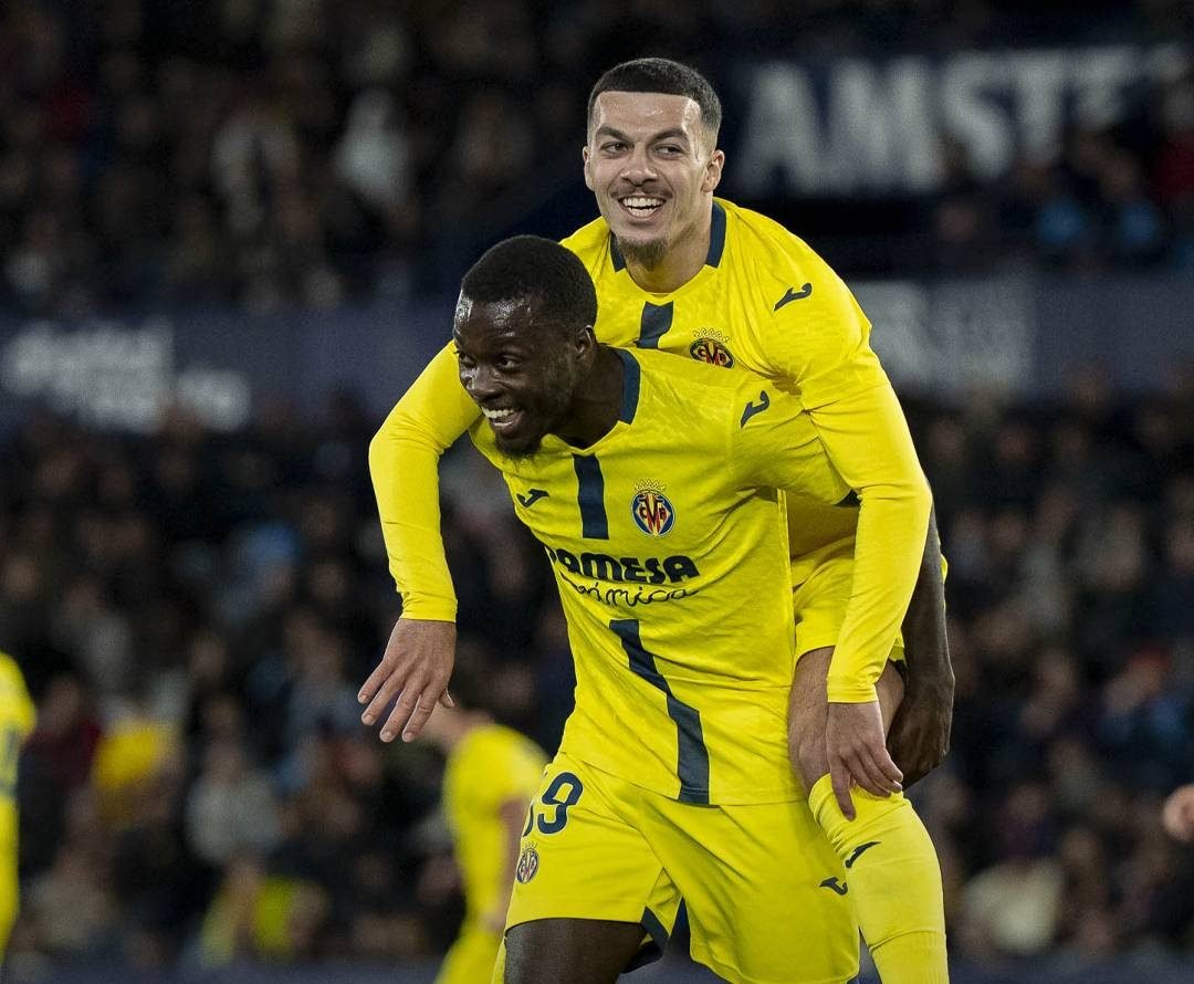Two Villarreal players celebrate a goal, one carrying the other on his shoulders on the pitch.