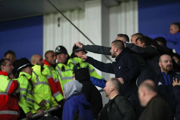 Stadium security in neon jackets confront a group of fans reaching out near a barrier.