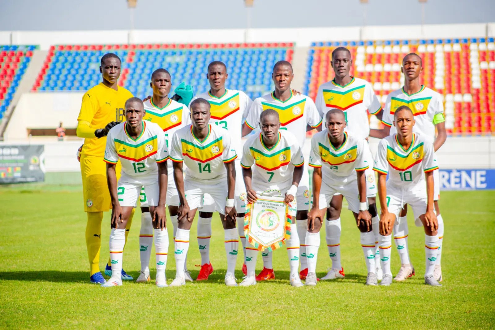 Senegal national football team posing for a group photo in white jerseys with green-yellow-red chevrons on a grass field.