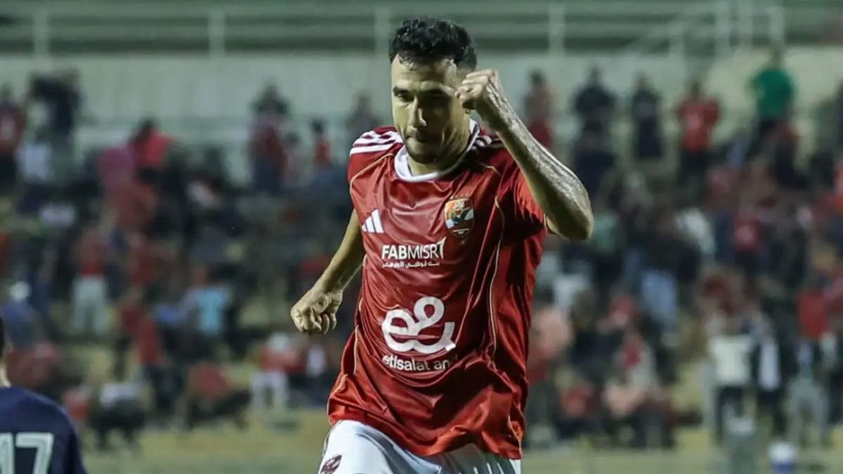 Soccer player in a red jersey celebrates with a raised fist on the field, crowds blurred in the background.