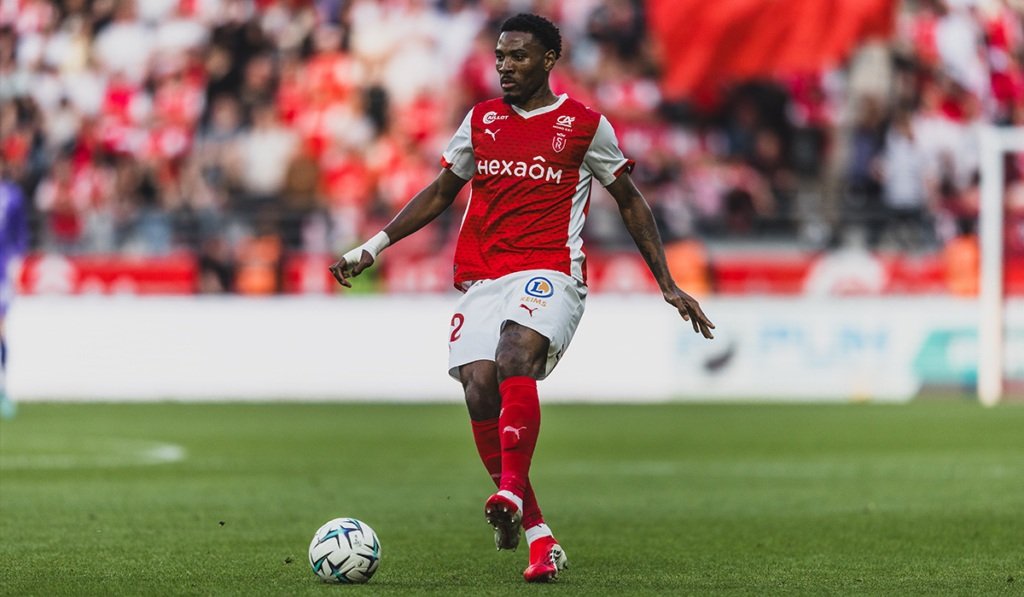 Soccer player in red and white kit dribbles with the ball on a green pitch, stadium crowd in the background. Soccer player in red and white kit dribbles with the ball on a green pitch, stadium crowd in the background.