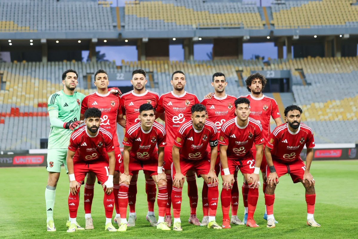 Soccer team in red uniforms posing for a group photo on the field with a goalkeeper in green at left.