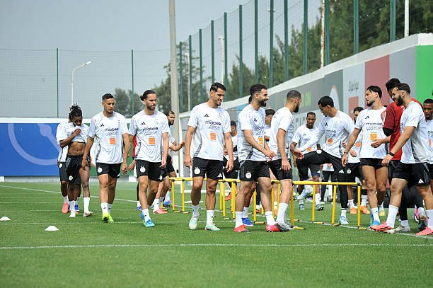 Soccer players in white training shirts line up behind yellow hurdles on a practice field during a drill. Soccer players in white training shirts line up behind yellow hurdles on a practice field during a drill.