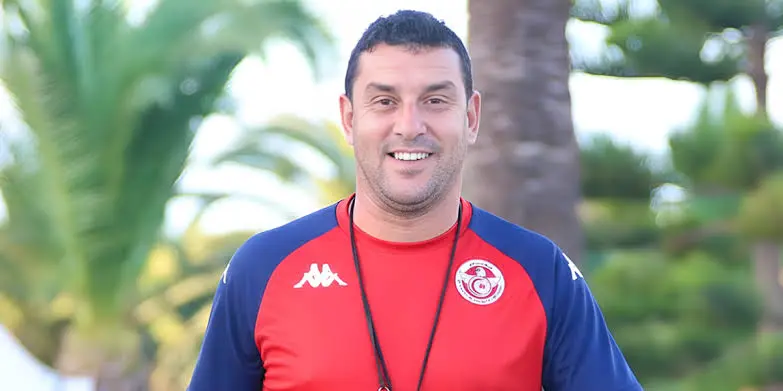 Smiling man in a red and blue athletic shirt outdoors with palm trees in the background, wearing a black lanyard. Smiling man in a red and blue athletic shirt outdoors with palm trees in the background, wearing a black lanyard.