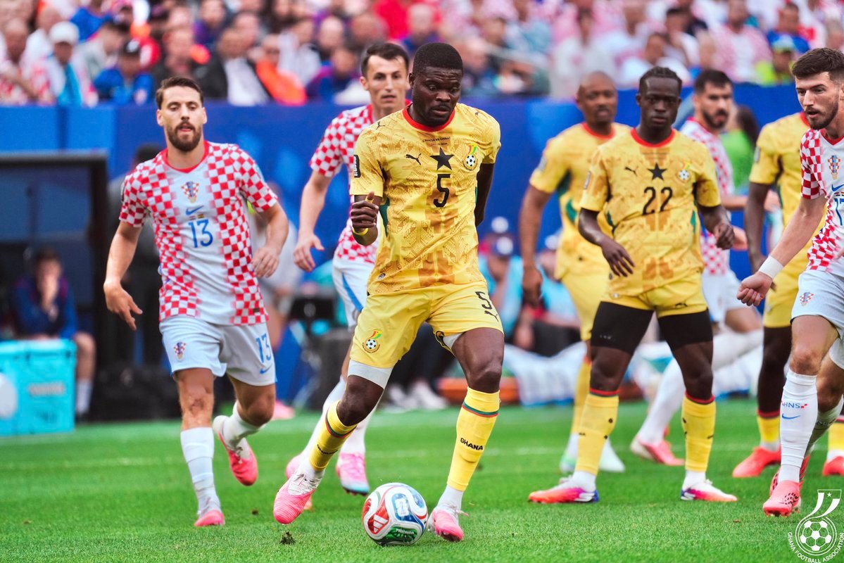 Soccer player in yellow Ghana jersey #5 dribbles the ball as Croatian opponents chase him on a green field. Soccer player in yellow Ghana jersey #5 dribbles the ball as Croatian opponents chase him on a green field.