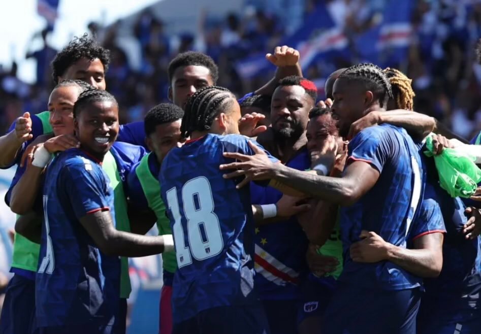 Soccer players in blue jerseys hug in a group celebration on the field after a match.