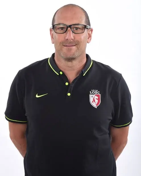 Portrait of a man in a black polo shirt with neon green trim and a Lille LOSC crest, facing the camera with hands behind his back. Portrait of a man in a black polo shirt with neon green trim and a Lille LOSC crest, facing the camera with hands behind his back.